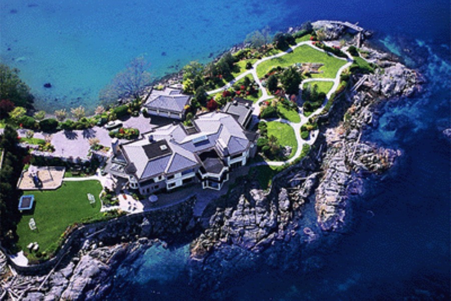An aerial view of a large residence and expansive property on a peninsula surrounded by blue water.