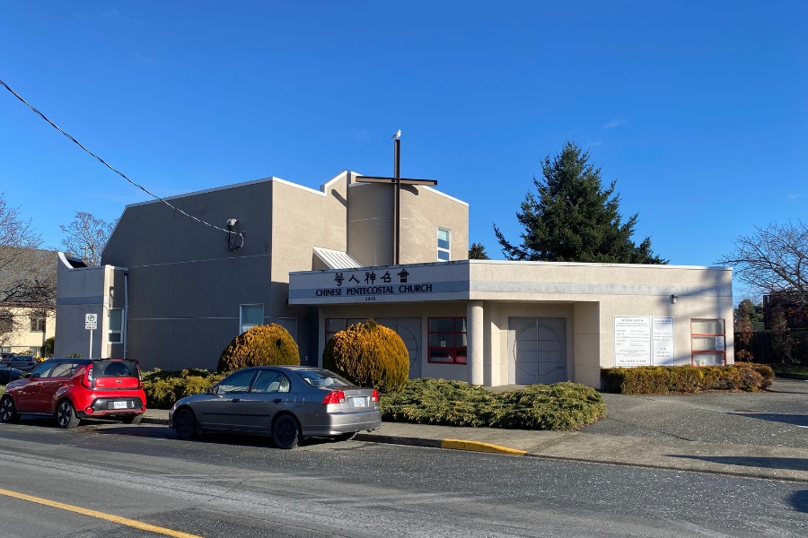 The exterior of Chinese Pentecostal Building, a commercial property, designed by Alan Lowe Architecture with light coloured siding and a cross above the signage.