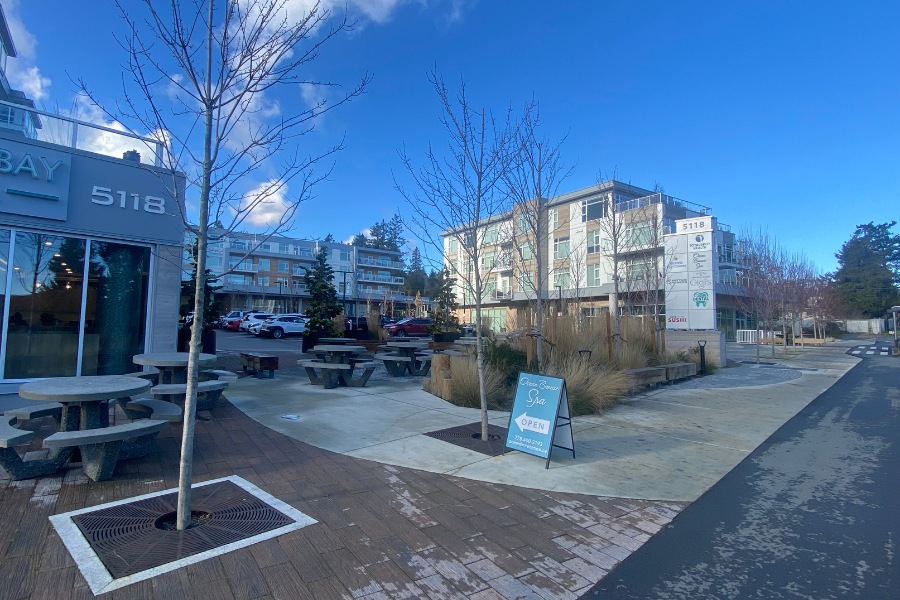 The exterior of Cordova Bay Shopping Center, a commercial property, designed by Alan Lowe Architecture with commercial spaces on the first level, a courtyard and parking lot in the center, and residential properties on the top three levels.