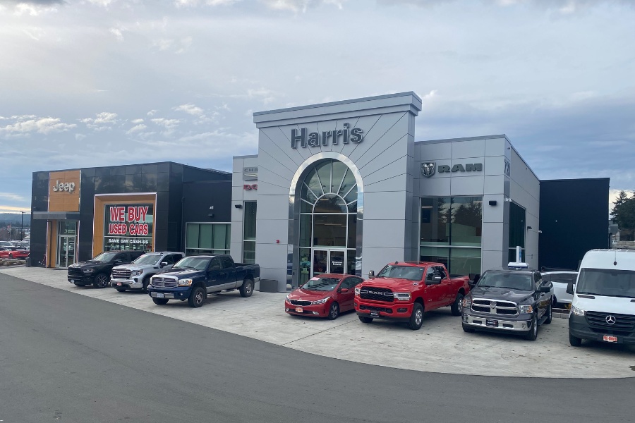 The exterior of Harris Dealership, a commercial property, designed by Alan Lowe Architecture with contemporary black and grey siding, wood accents, and a large glass exterior entrance.