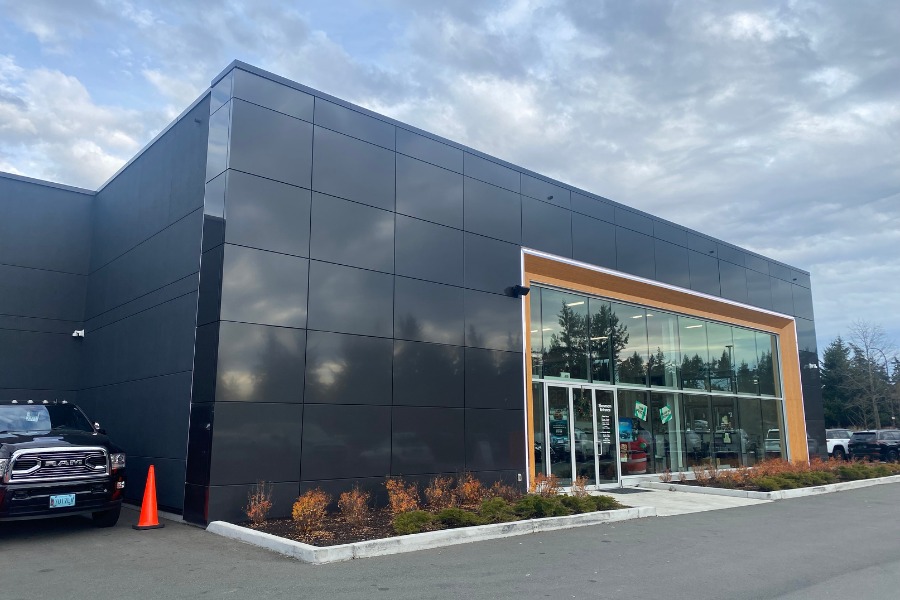 The exterior of Harris Dealership, a commercial property, designed by Alan Lowe Architecture with contemporary black siding, wood accents, and a large glass exterior entrance.