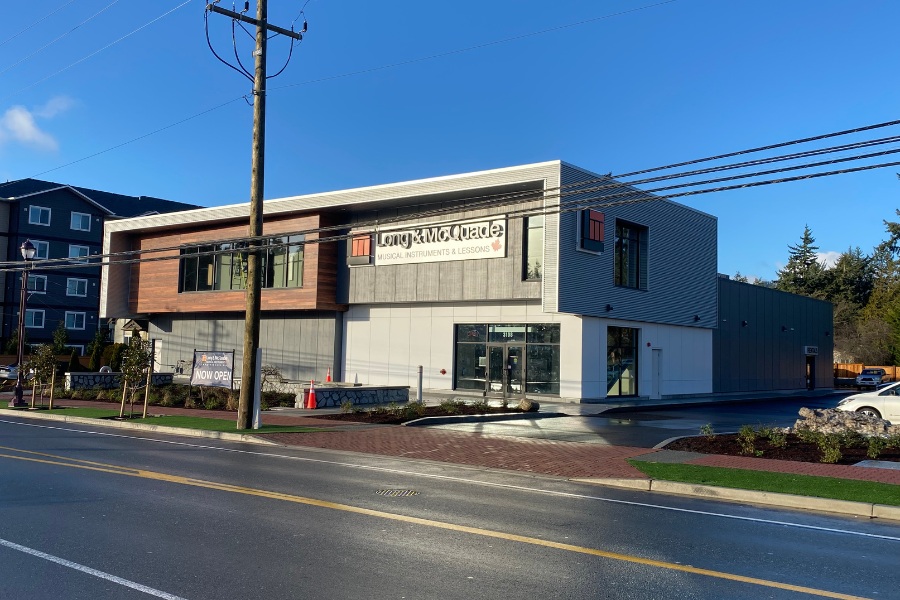 The exterior of Long & McQuade Building, a commercial property, designed by Alan Lowe Architecture with two levels, contemporary design with grey and horizontal wood siding.