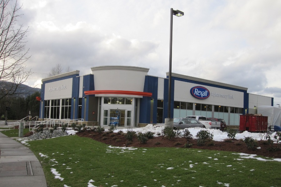 The exterior of a Rexall Pharmacy building, a commercial property, designed by Alan Lowe Architecture, with blue and white siding with red accents and big signage.